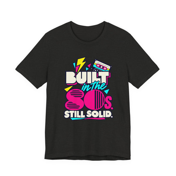 Built in the 80s. Still Solid Tee in Black Heather, front view with neon cassette design