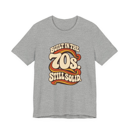 Built in the 70s. Still Solid Tee in Athletic Heather, front view with retro 70s lettering