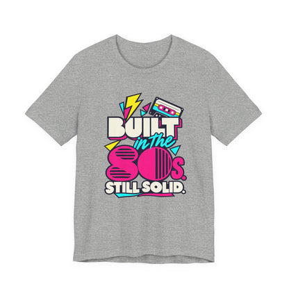 Built in the 80s. Still Solid Tee in Athletic Heather, front view with neon cassette design